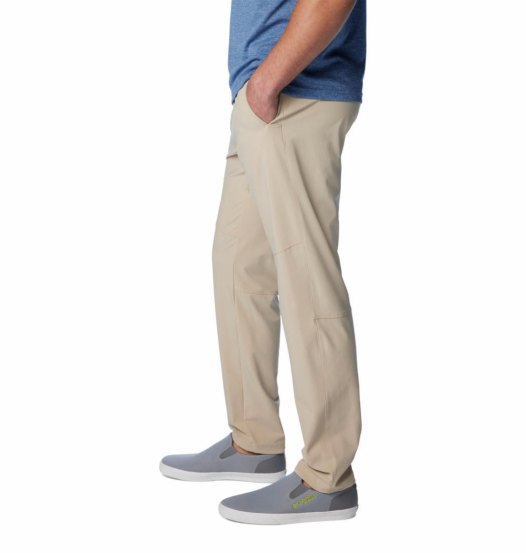 A man standing against a white background, wearing beige Columbia men's Omni-Shade Terminal Roamer Stretch Pant and a blue t-shirt with gray sneakers.