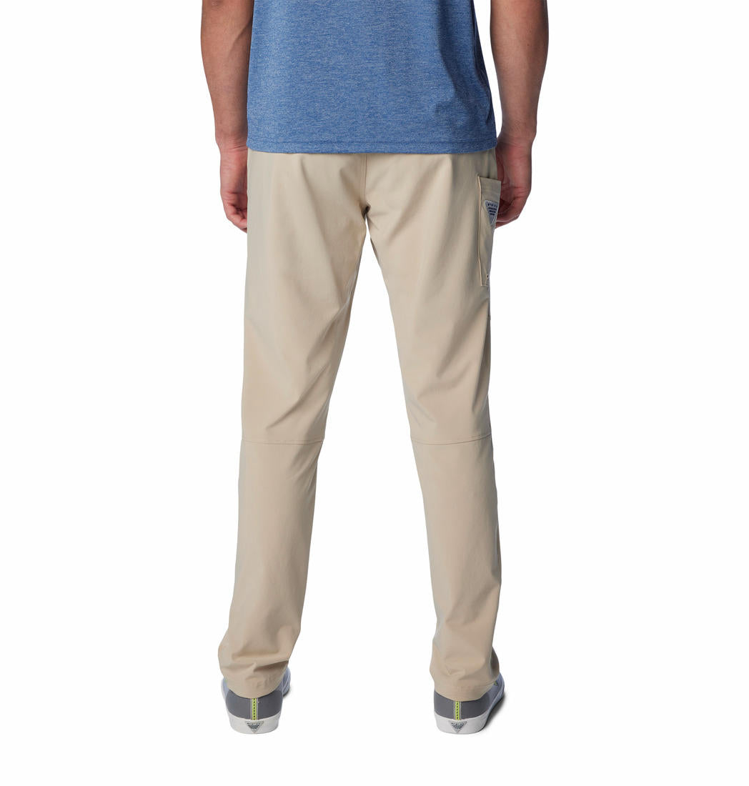 A man standing against a white background, wearing beige Columbia men's Omni-Shade Terminal Roamer Stretch Pant and a blue t-shirt with gray sneakers.